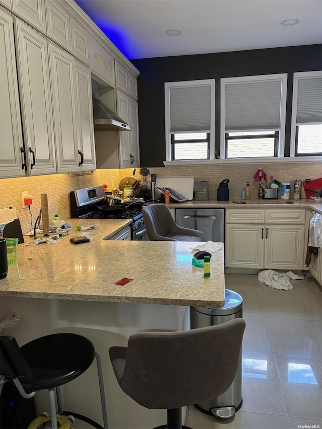 kitchen with wall chimney range hood, sink, appliances with stainless steel finishes, kitchen peninsula, and a breakfast bar area