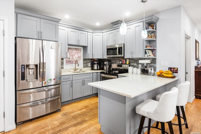 kitchen with kitchen peninsula, appliances with stainless steel finishes, sink, decorative light fixtures, and light hardwood / wood-style flooring