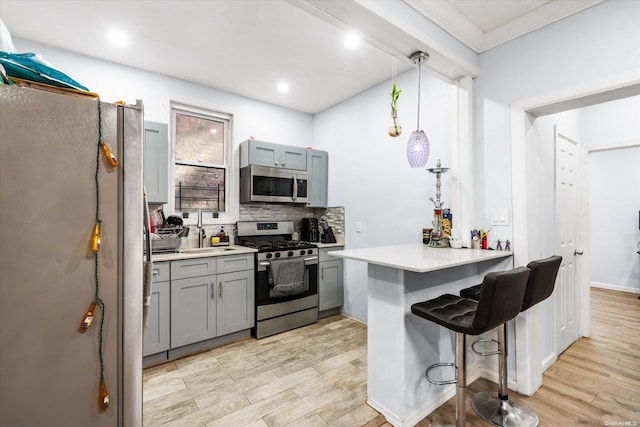 kitchen with a kitchen bar, appliances with stainless steel finishes, kitchen peninsula, light hardwood / wood-style flooring, and hanging light fixtures