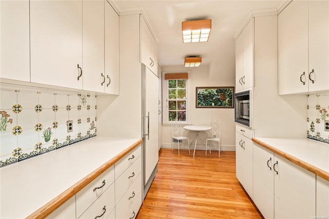 kitchen with tasteful backsplash, black microwave, white cabinetry, and light hardwood / wood-style floors