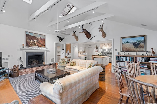 living room with ceiling fan, a fireplace, rail lighting, and light hardwood / wood-style flooring