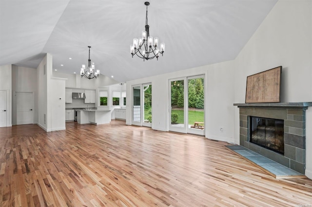 unfurnished living room with a tile fireplace, an inviting chandelier, vaulted ceiling, and light wood-type flooring