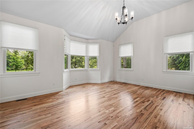 empty room featuring a notable chandelier, a healthy amount of sunlight, and light hardwood / wood-style flooring