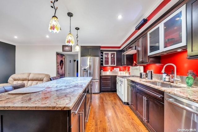 kitchen featuring sink, stainless steel appliances, pendant lighting, a kitchen island, and light wood-type flooring