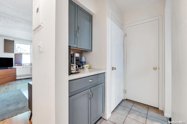 interior space featuring gray cabinetry, light tile patterned flooring, a textured ceiling, and a baseboard radiator