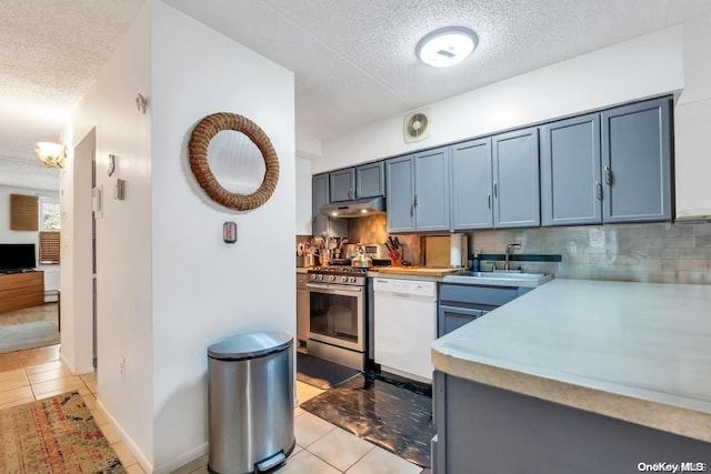 kitchen with stainless steel gas range oven, backsplash, white dishwasher, sink, and light tile patterned flooring