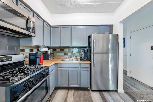 kitchen with gray cabinetry, sink, decorative backsplash, appliances with stainless steel finishes, and light hardwood / wood-style floors