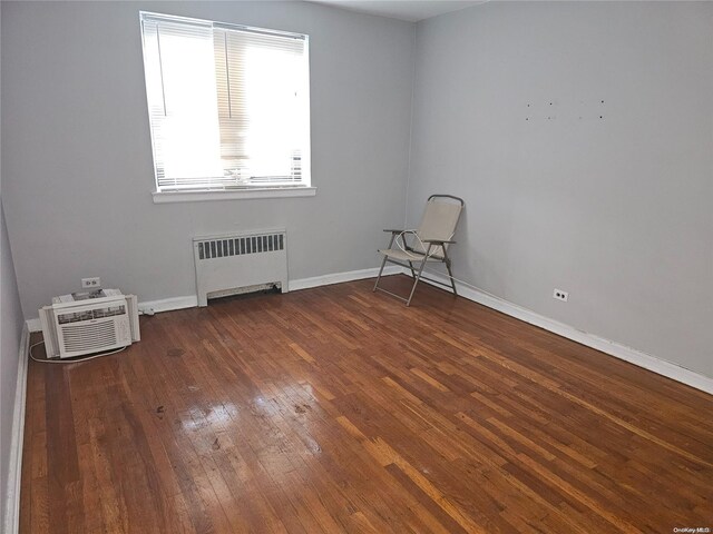 spare room featuring dark hardwood / wood-style floors, a wall unit AC, and radiator