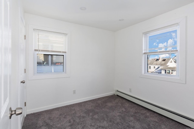 spare room with dark colored carpet and a baseboard heating unit