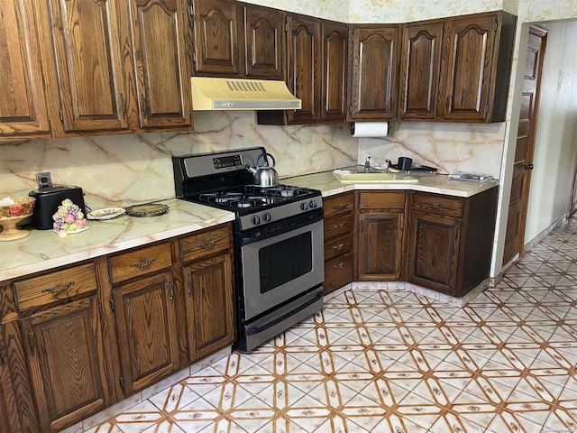 kitchen featuring ventilation hood, stainless steel gas stove, decorative backsplash, and sink