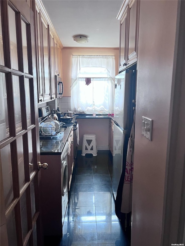 kitchen with ornamental molding, stainless steel appliances, dark tile patterned floors, dark stone countertops, and washer / dryer