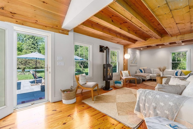 living room with beam ceiling, a wood stove, wood ceiling, and light wood-type flooring