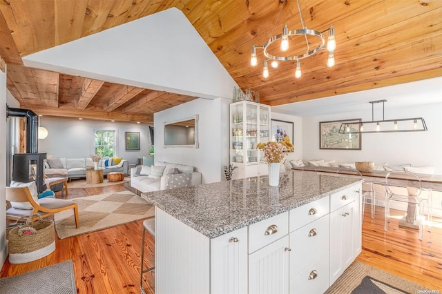 kitchen featuring wooden ceiling, dark stone counters, light hardwood / wood-style floors, a kitchen bar, and white cabinetry