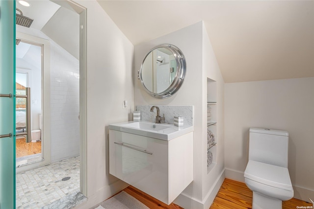 bathroom featuring vanity, vaulted ceiling, tiled shower, hardwood / wood-style floors, and toilet