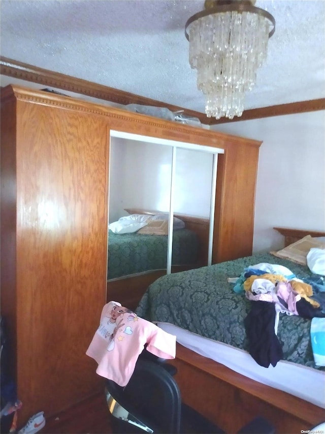 bedroom with crown molding, a closet, a textured ceiling, and a notable chandelier