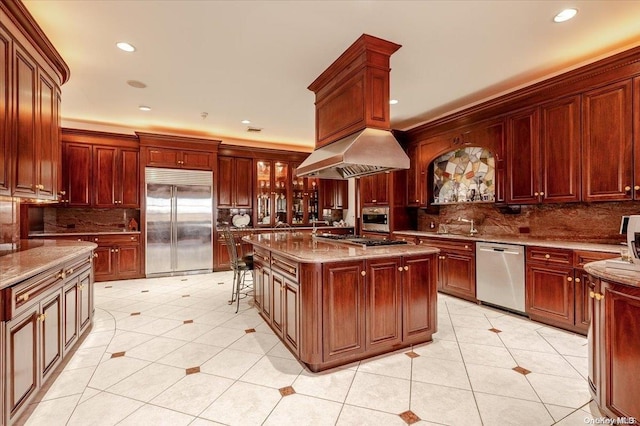 kitchen with light stone countertops, stainless steel appliances, island range hood, a center island, and light tile patterned flooring