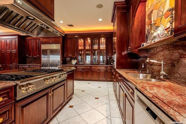 kitchen with sink, decorative backsplash, light stone counters, custom range hood, and stainless steel appliances