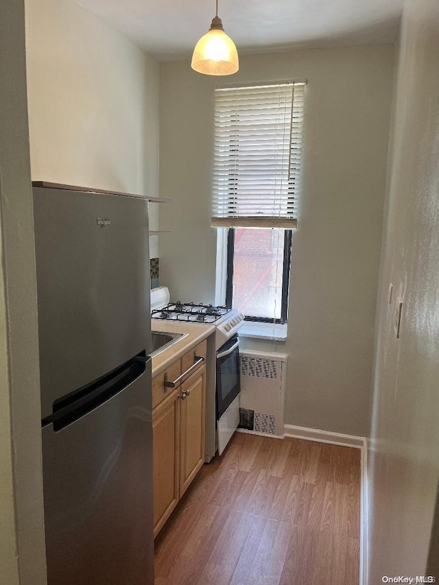 kitchen featuring stainless steel fridge, white gas range oven, pendant lighting, light brown cabinets, and light hardwood / wood-style flooring