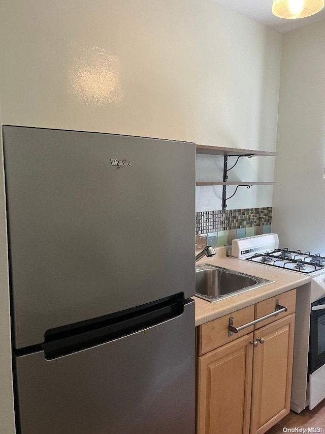 kitchen featuring white gas range, sink, light brown cabinets, stainless steel fridge, and light hardwood / wood-style floors