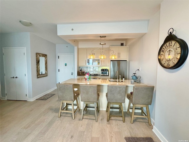 kitchen featuring stainless steel refrigerator, sink, light hardwood / wood-style flooring, decorative light fixtures, and a breakfast bar