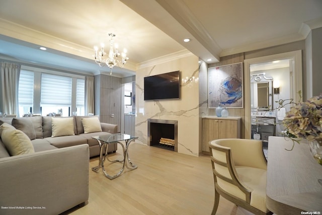 living room featuring a high end fireplace, light hardwood / wood-style floors, an inviting chandelier, and ornamental molding