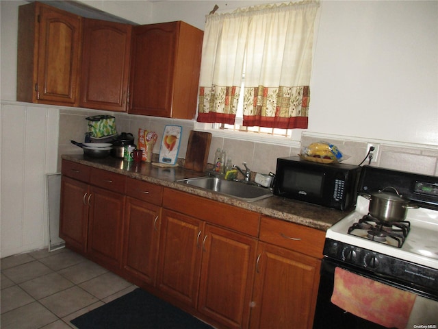 kitchen featuring backsplash, white gas stove, light tile patterned floors, and sink