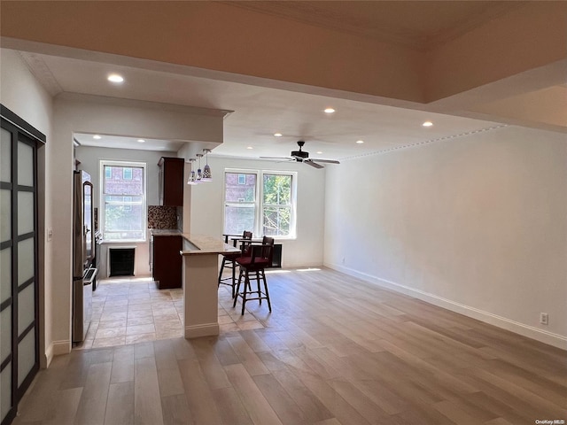 kitchen featuring backsplash, a kitchen breakfast bar, hanging light fixtures, ceiling fan, and light wood-type flooring