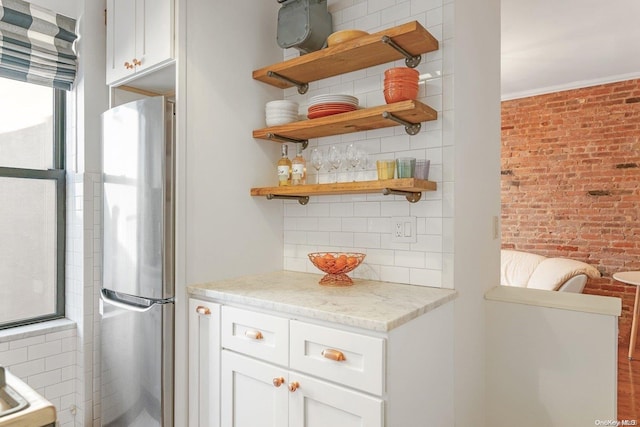 bar featuring brick wall, light stone counters, white cabinetry, and stainless steel refrigerator