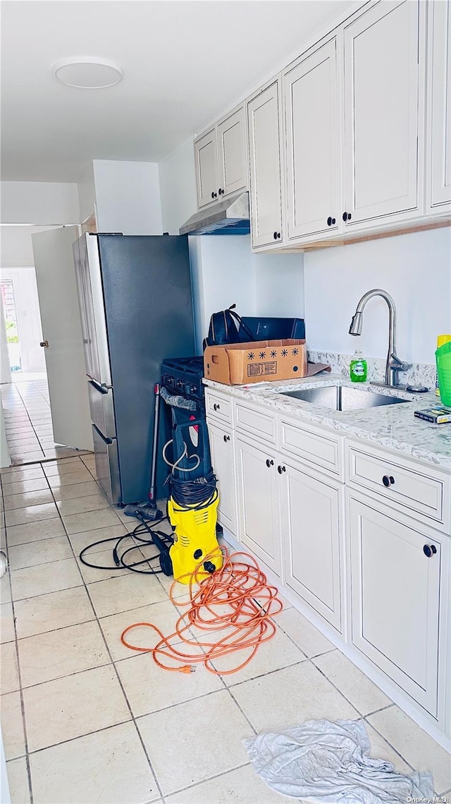 kitchen featuring white cabinets, sink, light stone countertops, light tile patterned floors, and stainless steel refrigerator