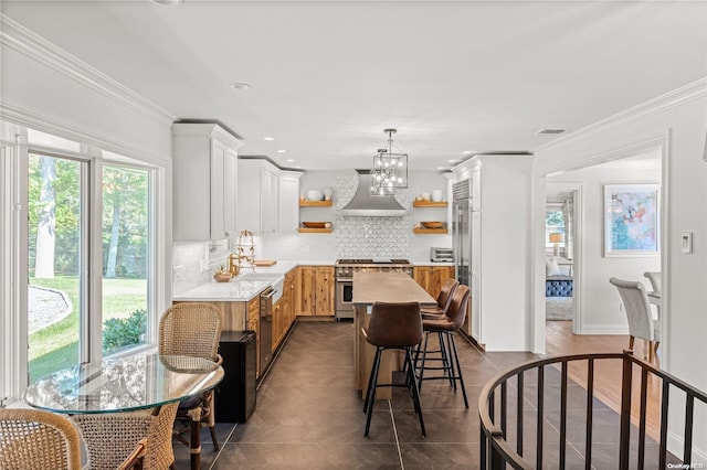 kitchen with backsplash, wall chimney range hood, hanging light fixtures, crown molding, and appliances with stainless steel finishes