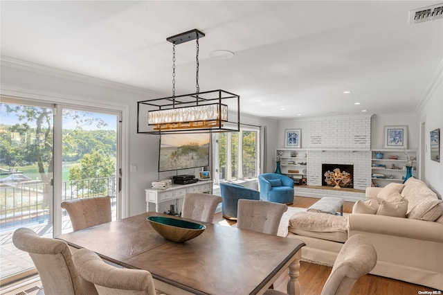 dining area featuring hardwood / wood-style floors, a healthy amount of sunlight, ornamental molding, and a brick fireplace