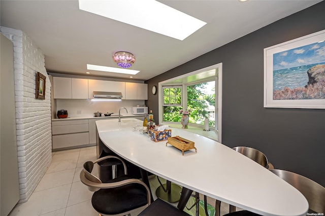 kitchen featuring a skylight, white cabinetry, sink, extractor fan, and light tile patterned floors