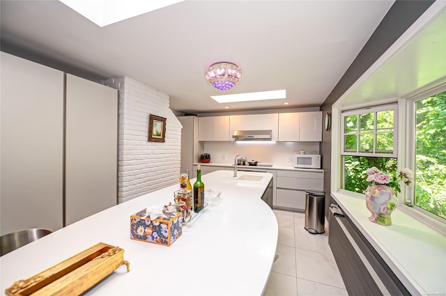 kitchen featuring a skylight, ventilation hood, light tile patterned floors, stovetop, and white cabinets