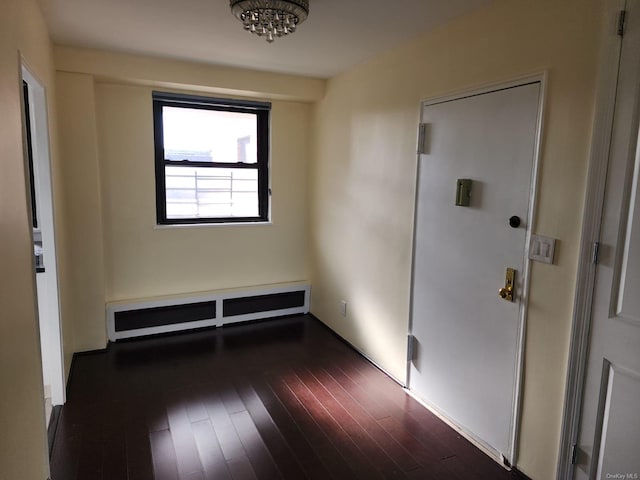 spare room featuring dark wood-style floors, a chandelier, and a baseboard radiator