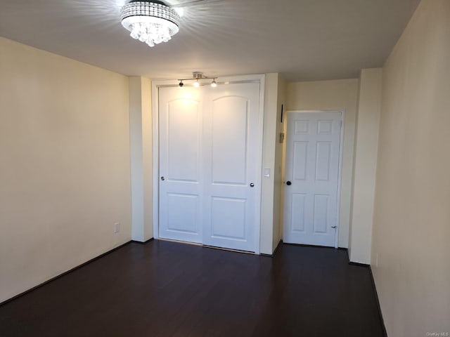 unfurnished bedroom featuring a closet, a chandelier, dark wood-type flooring, and baseboards