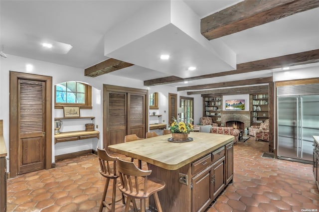 kitchen featuring wood counters, a kitchen breakfast bar, stainless steel built in fridge, beamed ceiling, and a center island