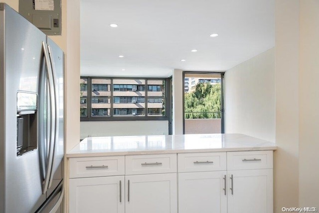 kitchen with white cabinets, stainless steel fridge with ice dispenser, kitchen peninsula, and light stone counters