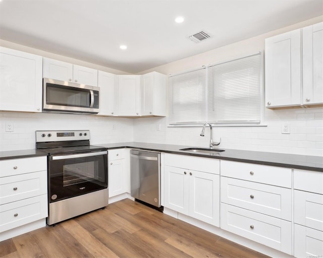 kitchen featuring appliances with stainless steel finishes, tasteful backsplash, sink, wood-type flooring, and white cabinets