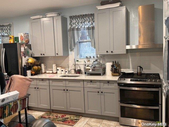 kitchen with decorative backsplash, gray cabinetry, wall chimney exhaust hood, sink, and stainless steel stove