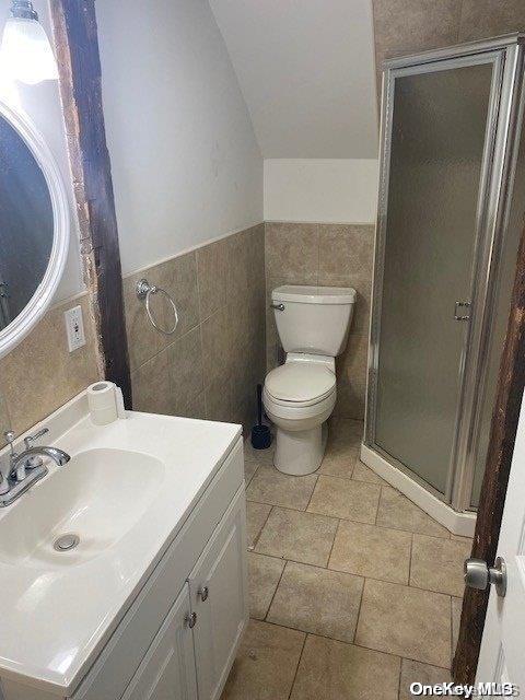 bathroom with an enclosed shower, vanity, toilet, and tile walls