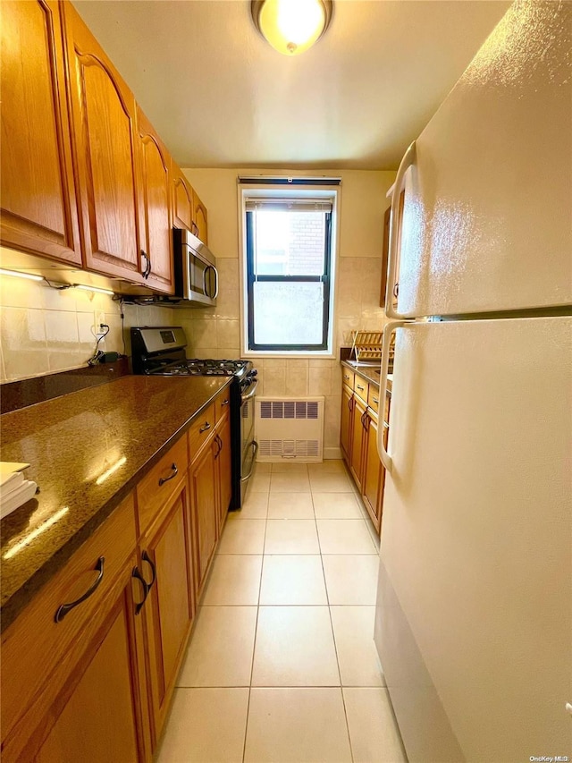 kitchen featuring light tile patterned flooring, backsplash, black range with gas stovetop, dark stone countertops, and white fridge