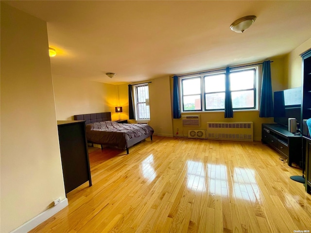 bedroom featuring radiator heating unit, light hardwood / wood-style flooring, multiple windows, and an AC wall unit