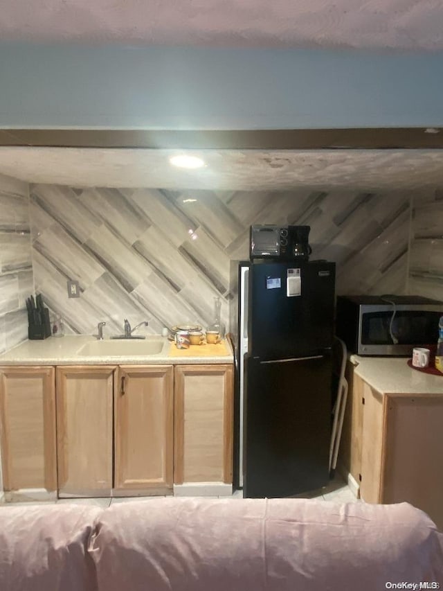 kitchen featuring black refrigerator, sink, wooden walls, vaulted ceiling, and light brown cabinetry