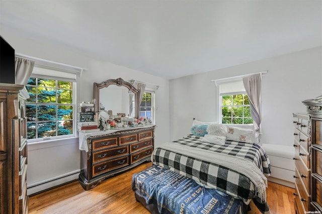 bedroom with light hardwood / wood-style flooring, multiple windows, and a baseboard heating unit