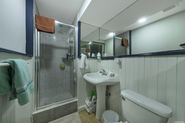 bathroom with tile patterned floors, wood walls, toilet, and a shower with shower door