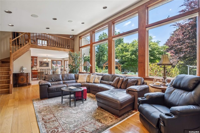 living room featuring a chandelier, a towering ceiling, a wealth of natural light, and light hardwood / wood-style flooring