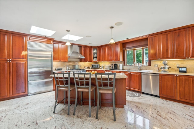 kitchen with a skylight, sink, wall chimney exhaust hood, stainless steel appliances, and decorative light fixtures