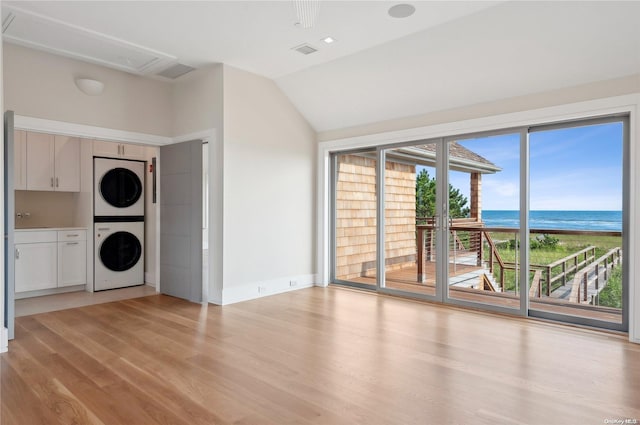 451 Dune Rd, Westhampton Beach, NY 11978 - unfurnished living room featuring stacked washer / drying machine, a water view, light wood-style floors, vaulted ceiling, and attic access