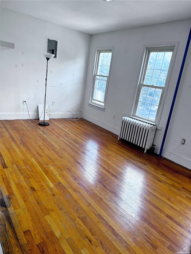 unfurnished room with hardwood / wood-style flooring, radiator, and a healthy amount of sunlight