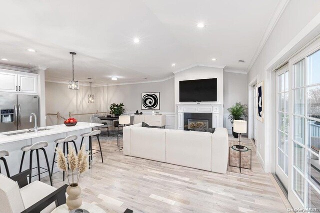 living room featuring ornamental molding, sink, a notable chandelier, light hardwood / wood-style floors, and lofted ceiling